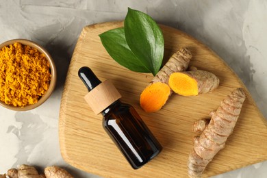 Photo of Turmeric oil, roots, powder and green leaves on grey textured table, flat lay