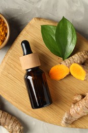 Photo of Turmeric oil, roots, powder and green leaves on grey textured table, flat lay