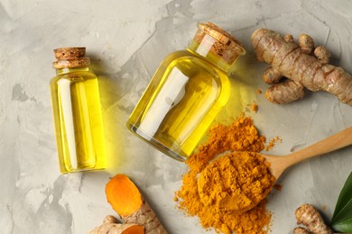 Photo of Turmeric oil, roots and powder on grey textured table, flat lay