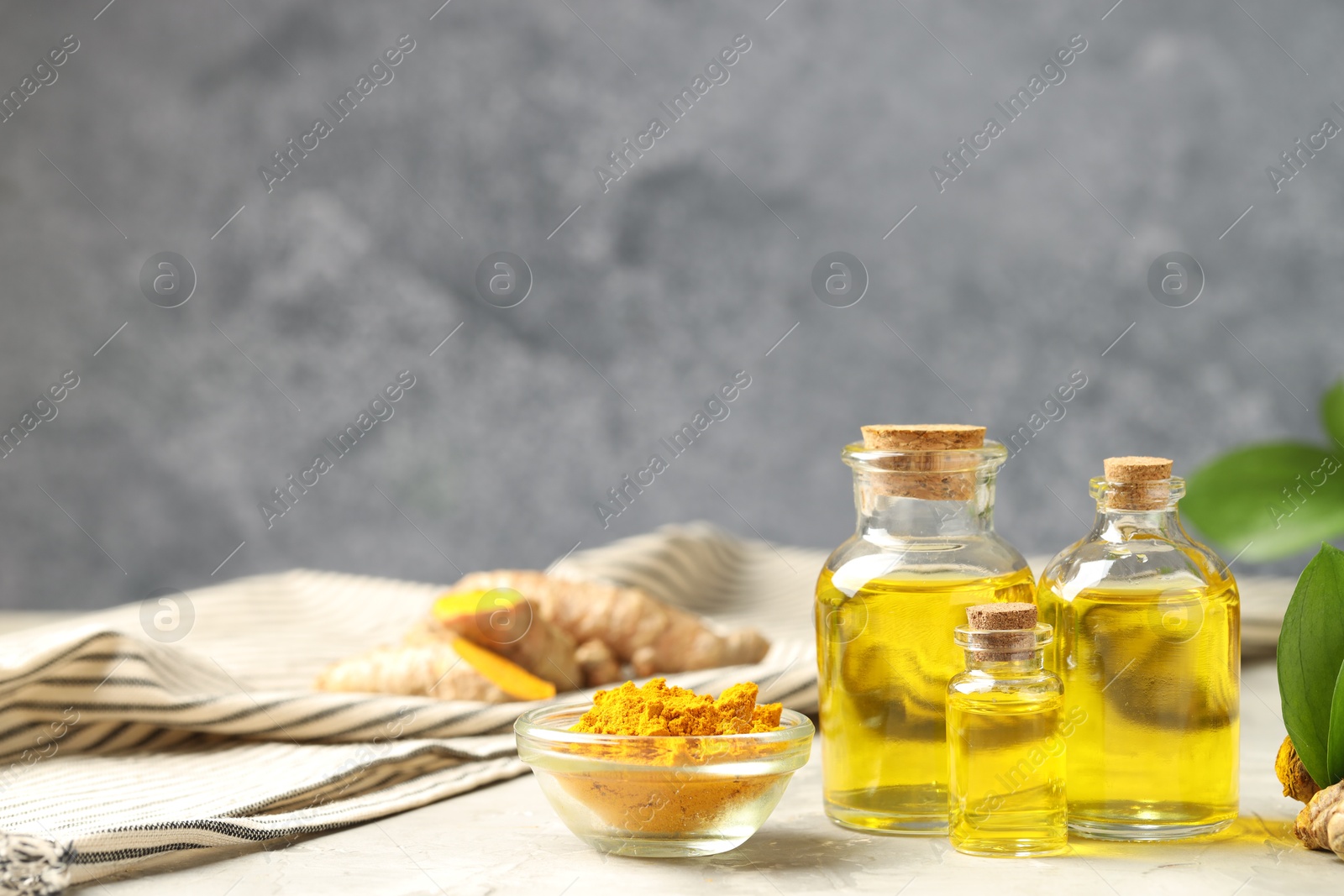 Photo of Turmeric oil, powder green leaves on grey table, space for text