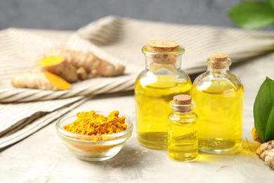 Photo of Turmeric oil, powder and green leaves on grey table, closeup