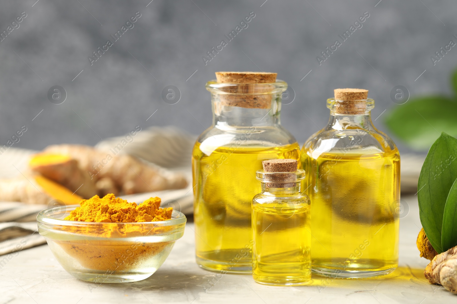 Photo of Turmeric oil, powder and green leaves on grey table, closeup