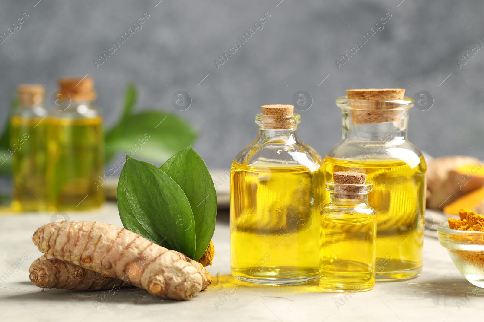 Photo of Turmeric oil, powder, roots and green leaves on grey table, closeup