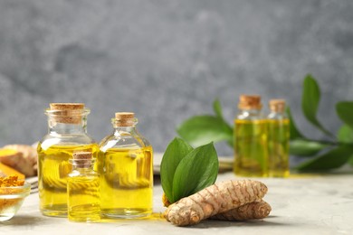 Photo of Turmeric oil, powder, roots and green leaves on grey table