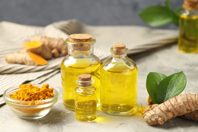 Photo of Turmeric oil, powder, roots and green leaves on grey table, closeup