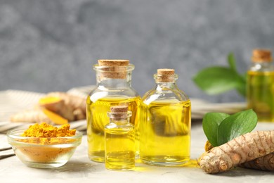 Photo of Turmeric oil, powder, roots and green leaves on grey table