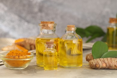 Photo of Turmeric oil, powder, roots and green leaves on grey table