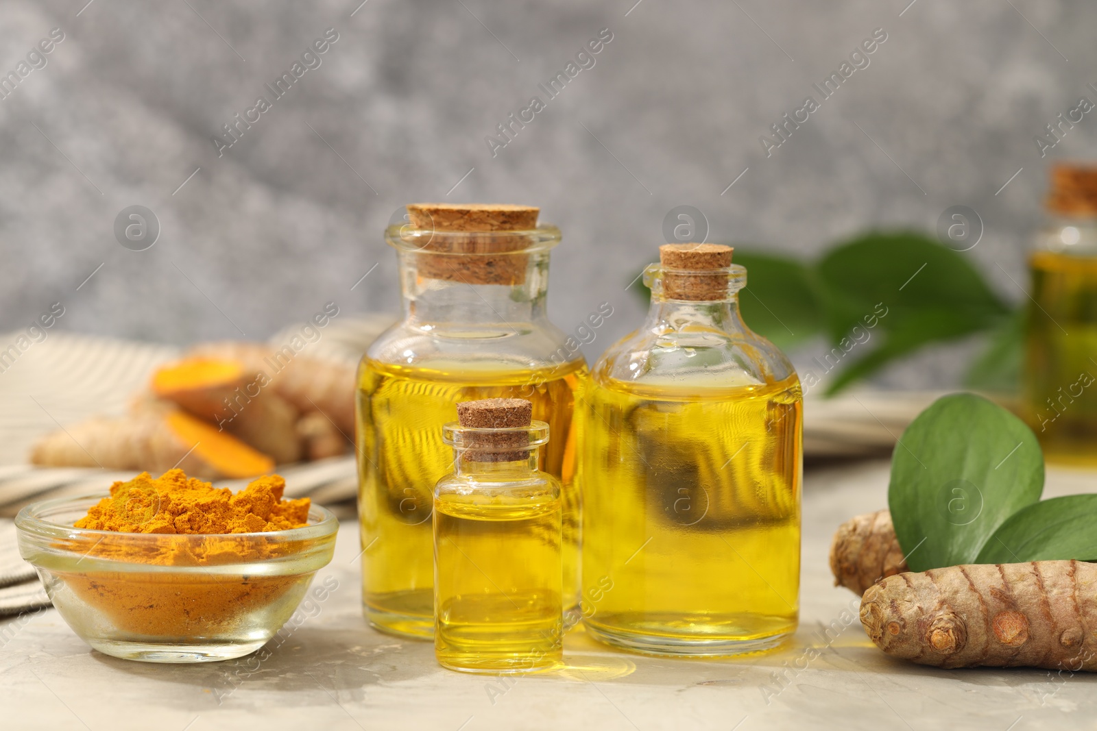 Photo of Turmeric oil, powder, roots and green leaves on grey table