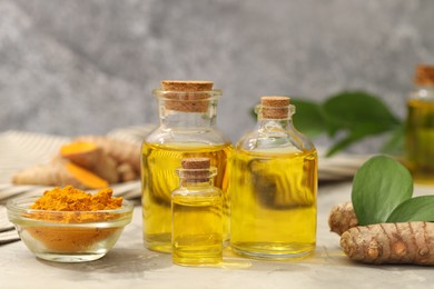 Photo of Turmeric oil, powder, roots and green leaves on grey table