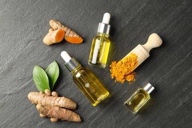 Photo of Turmeric oil, powder, roots and green leaves on black table, flat lay