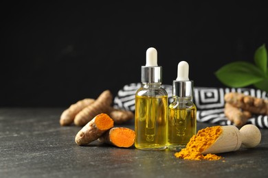 Photo of Turmeric oil, powder and roots on black table, space for text