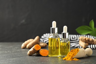 Photo of Turmeric oil, powder and roots on black table, space for text