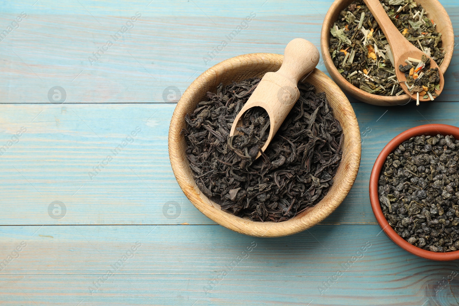 Photo of Different dry tea leaves in bowls on light blue wooden table, flat lay. Space for text