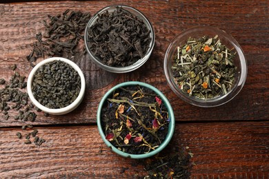 Photo of Different dry tea leaves in bowl on wooden table, flat lay