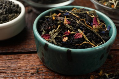 Photo of Different dry tea leaves in bowl on wooden table, closeup