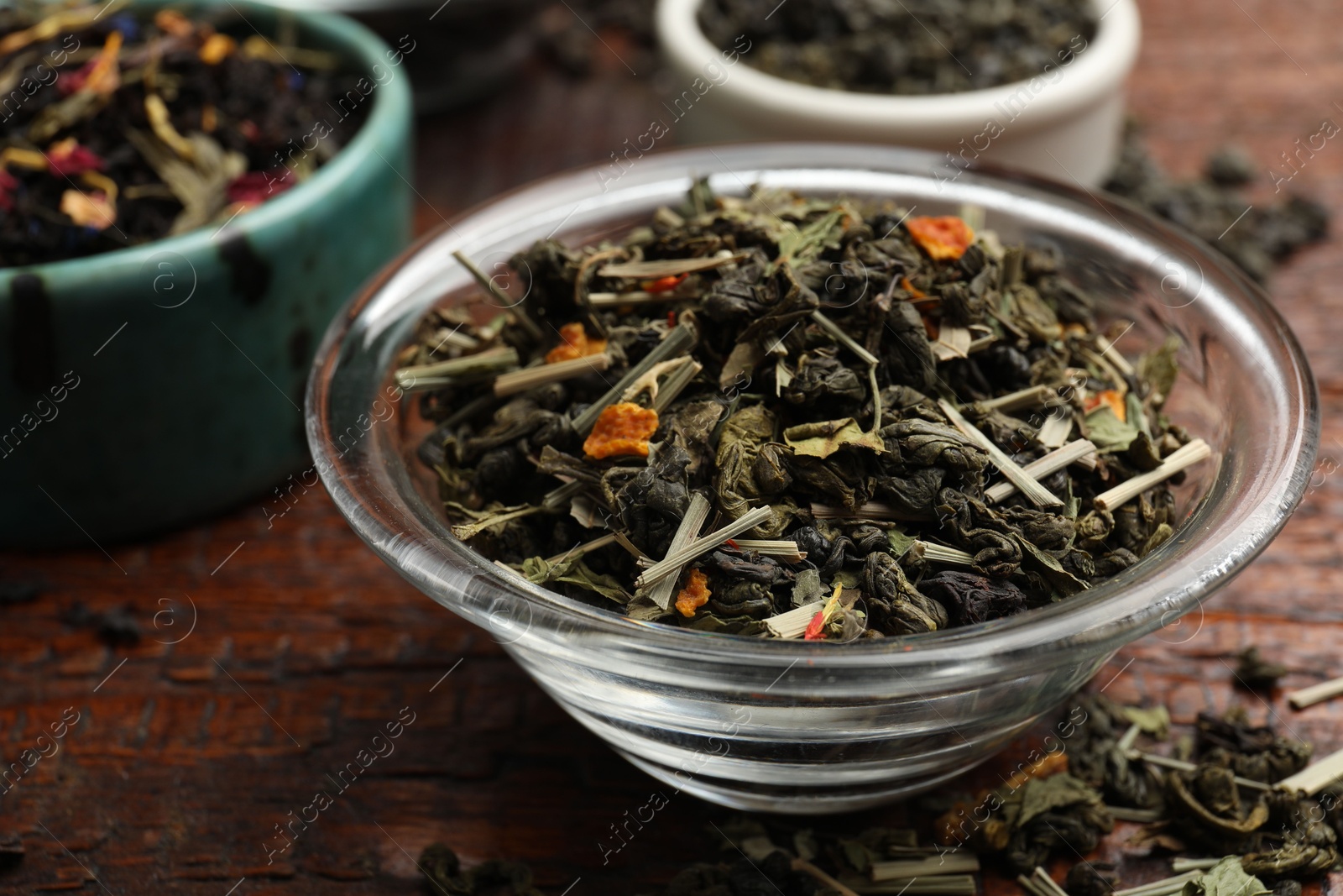 Photo of Different dry tea leaves in bowl on wooden table, closeup