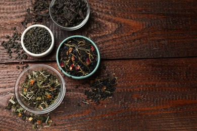 Photo of Different dry tea leaves in bowl on wooden table, flat lay