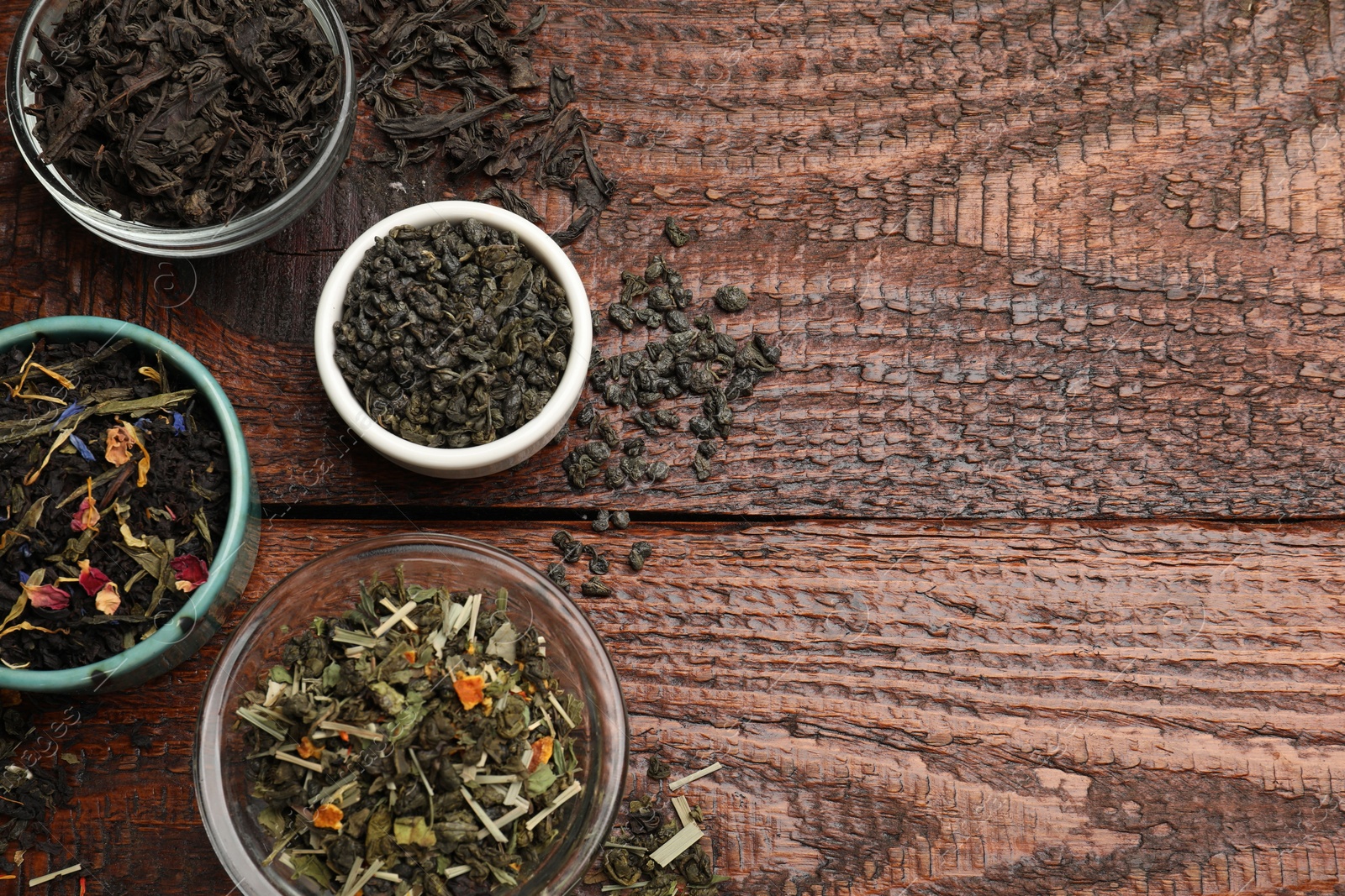 Photo of Different dry tea leaves in bowl on wooden table, flat lay. Space for text