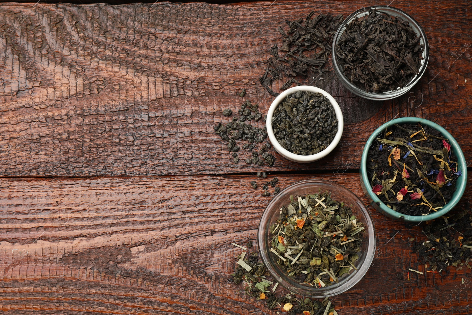 Photo of Different dry tea leaves in bowl on wooden table, flat lay. Space for text