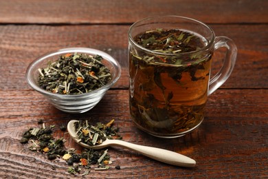 Photo of Aromatic tea in glass cup and dry leaves on wooden table, closeup