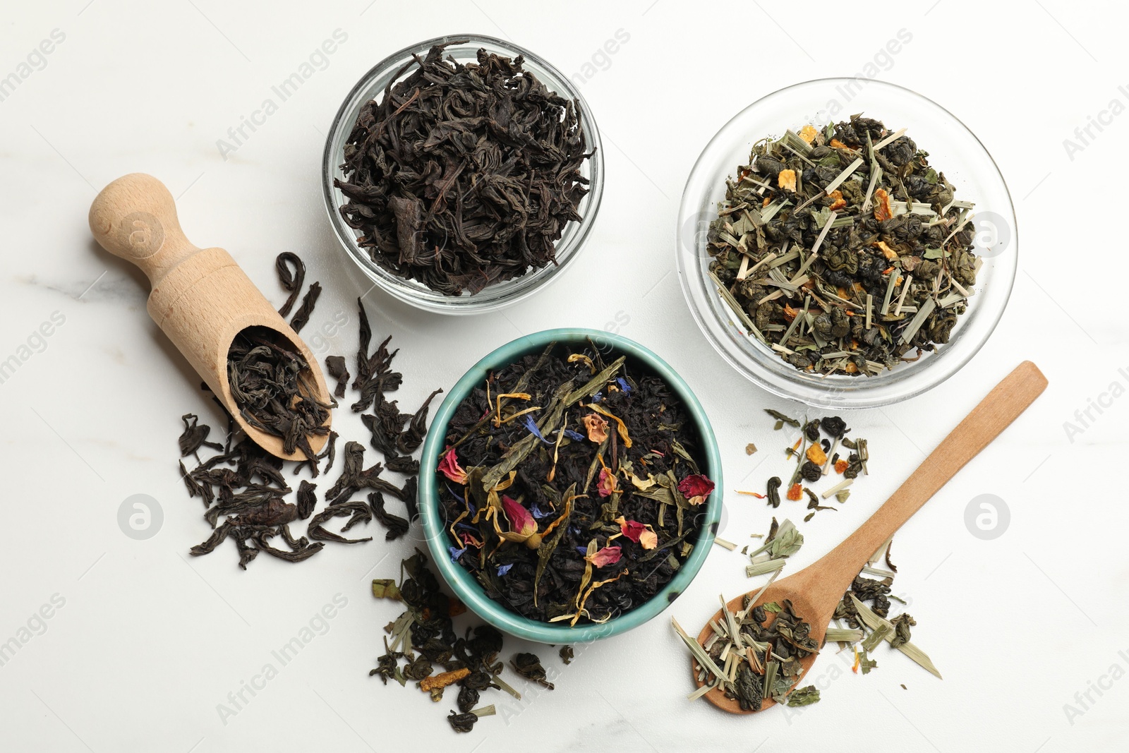 Photo of Different dry tea leaves on white marble table, flat lay