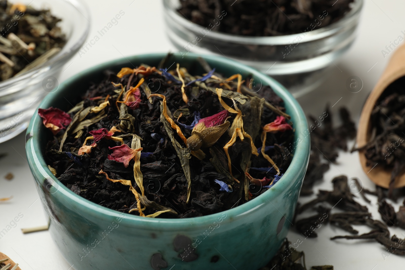 Photo of Different dry tea leaves in bowls on white table, closeup