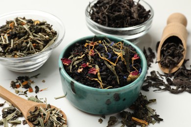 Photo of Different dry tea leaves on white table, closeup