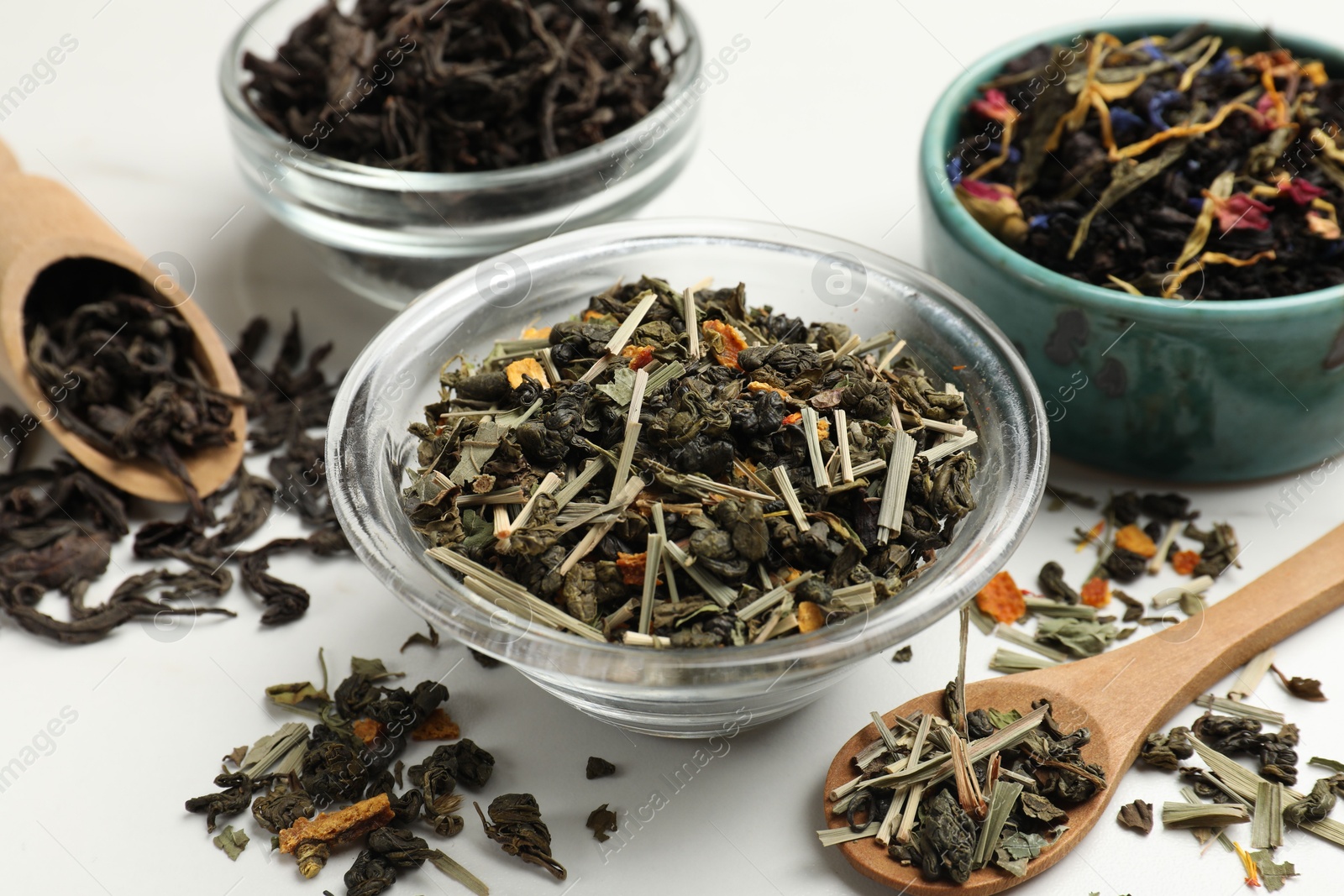 Photo of Different dry tea leaves on white table, closeup