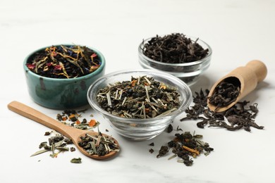 Photo of Different dry tea leaves on white marble table, closeup