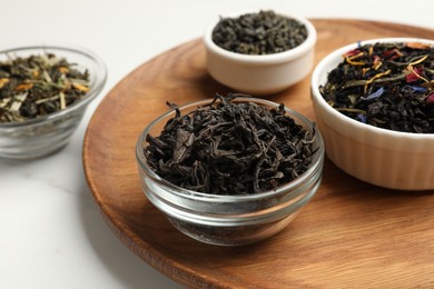 Photo of Different dry tea leaves in bowls on white marble table, closeup