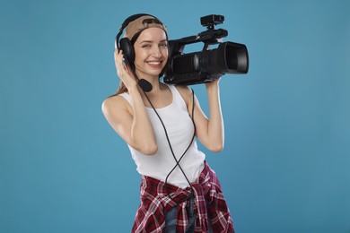 Photo of Happy woman with professional video camera and headset on light blue background