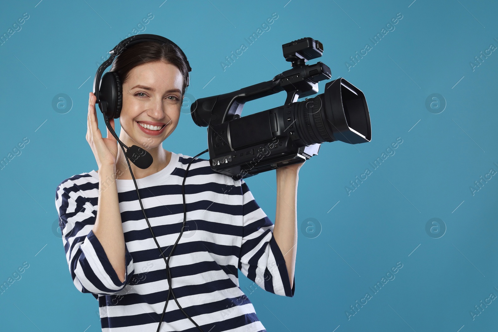 Photo of Happy woman with professional video camera and headset on light blue background, space for text