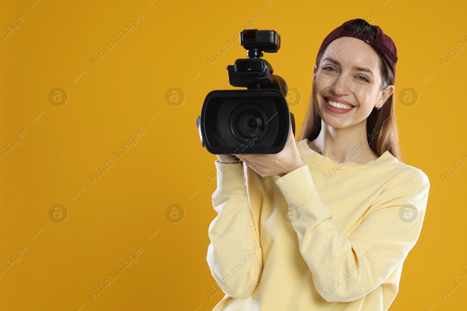 Photo of Happy woman with professional video camera on orange background, space for text