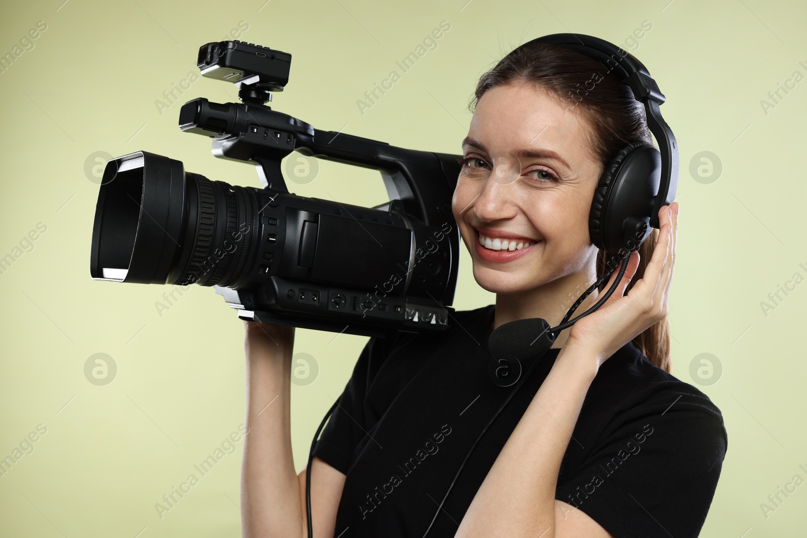 Photo of Happy woman with professional video camera and headset on pale olive background