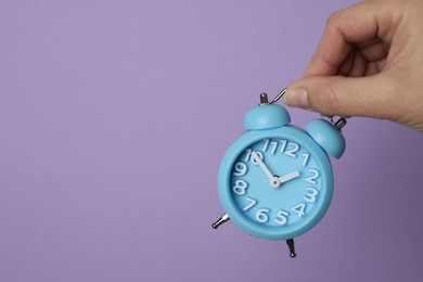 Photo of Woman with alarm clock on lilac background, closeup. Space for text