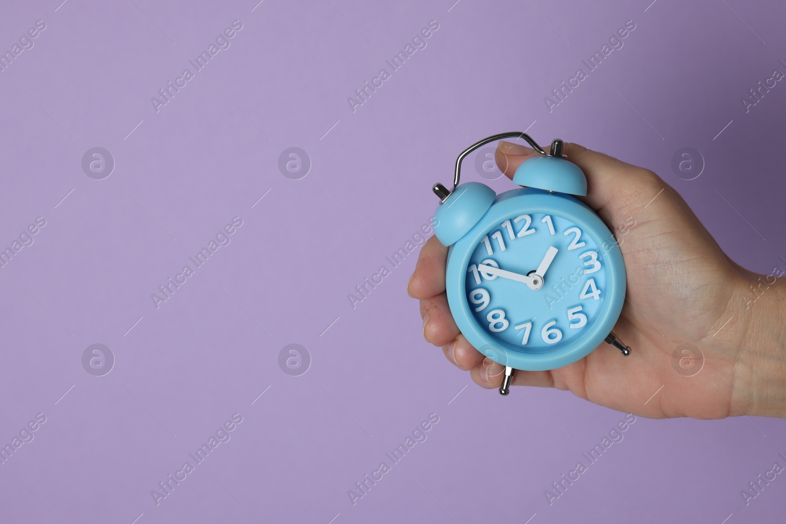 Photo of Woman with alarm clock on lilac background, closeup. Space for text