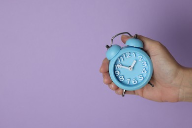 Photo of Woman with alarm clock on lilac background, closeup. Space for text