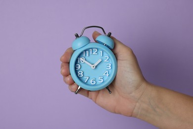 Woman with alarm clock on lilac background, closeup