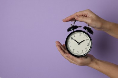 Woman with alarm clock on lilac background, closeup. Space for text