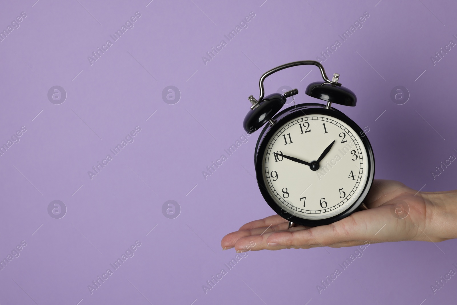 Photo of Woman with alarm clock on lilac background, closeup. Space for text