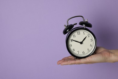 Woman with alarm clock on lilac background, closeup. Space for text