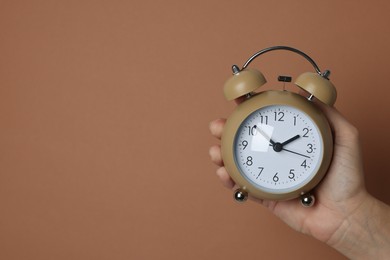 Photo of Woman with alarm clock on brown background, closeup. Space for text