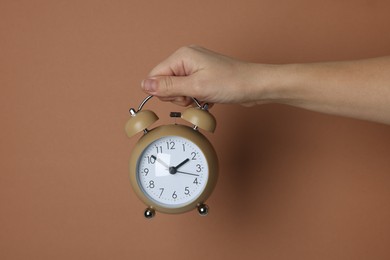 Photo of Woman with alarm clock on brown background, closeup