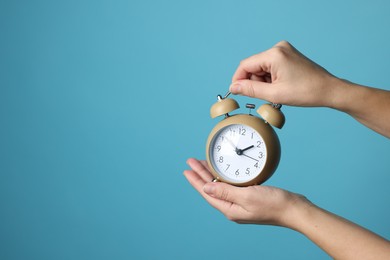 Woman with alarm clock on blue background, closeup. Space for text