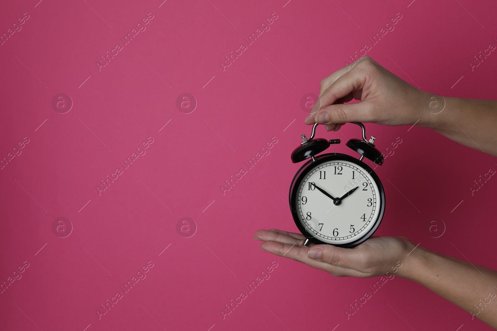 Photo of Woman with alarm clock on crimson background, closeup. Space for text