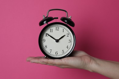 Woman with alarm clock on crimson background, closeup