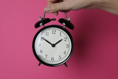 Woman with alarm clock on crimson background, closeup