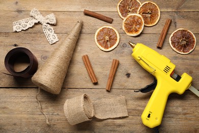 Photo of Hot glue gun and handicraft materials on wooden background, flat lay