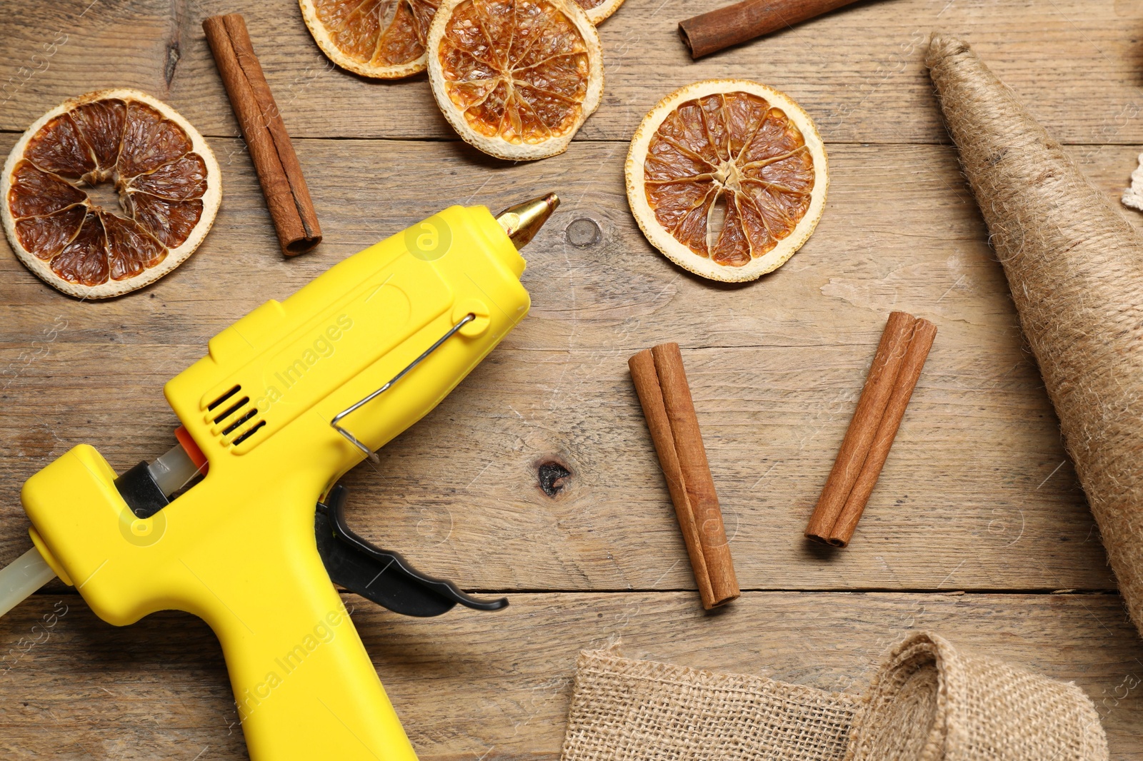 Photo of Hot glue gun and handicraft materials on wooden background, flat lay