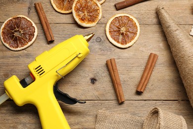 Photo of Hot glue gun and handicraft materials on wooden background, flat lay